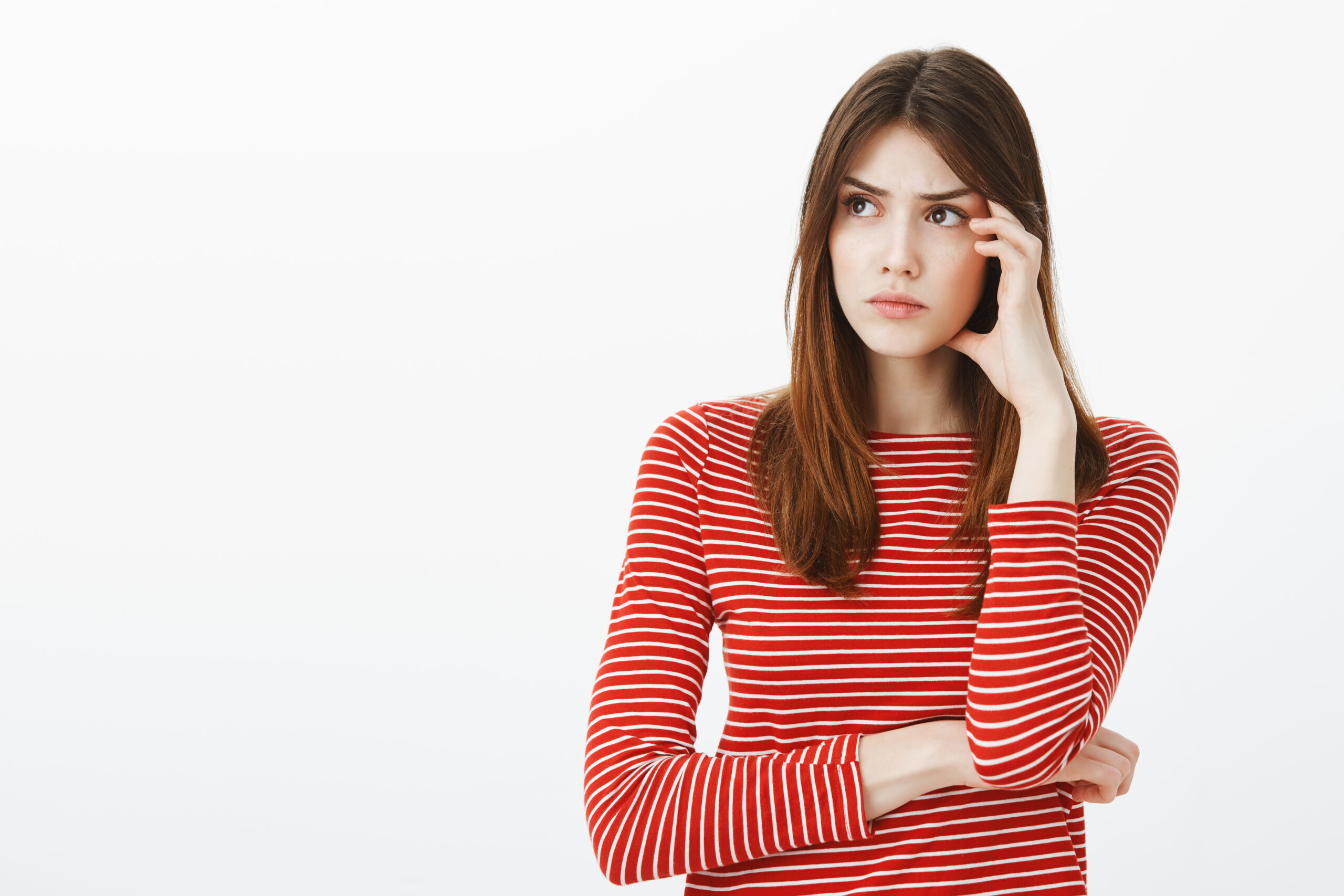 Keep thinking and ideas will come. Portrait of focused attractive smart woman in striped clothes, looking aside and touching temple, carried away with thoughts, recalling important moment over thinking