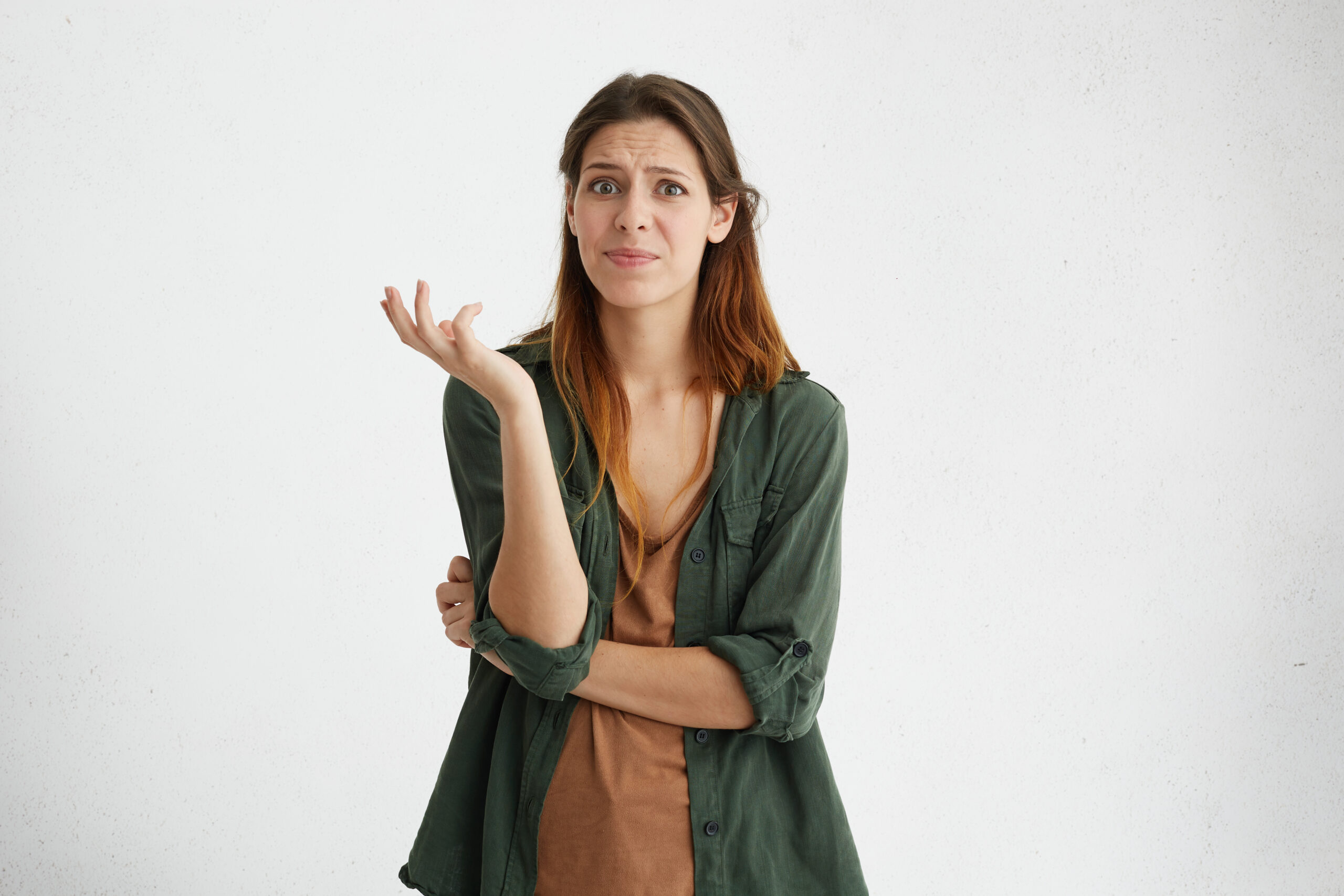 What? Casually dressed puzzled female standing at blank studio wall, having questionable look, her facial emotions and gesture expressing indignation, dislike and uncertainty towards something negativety thinking
